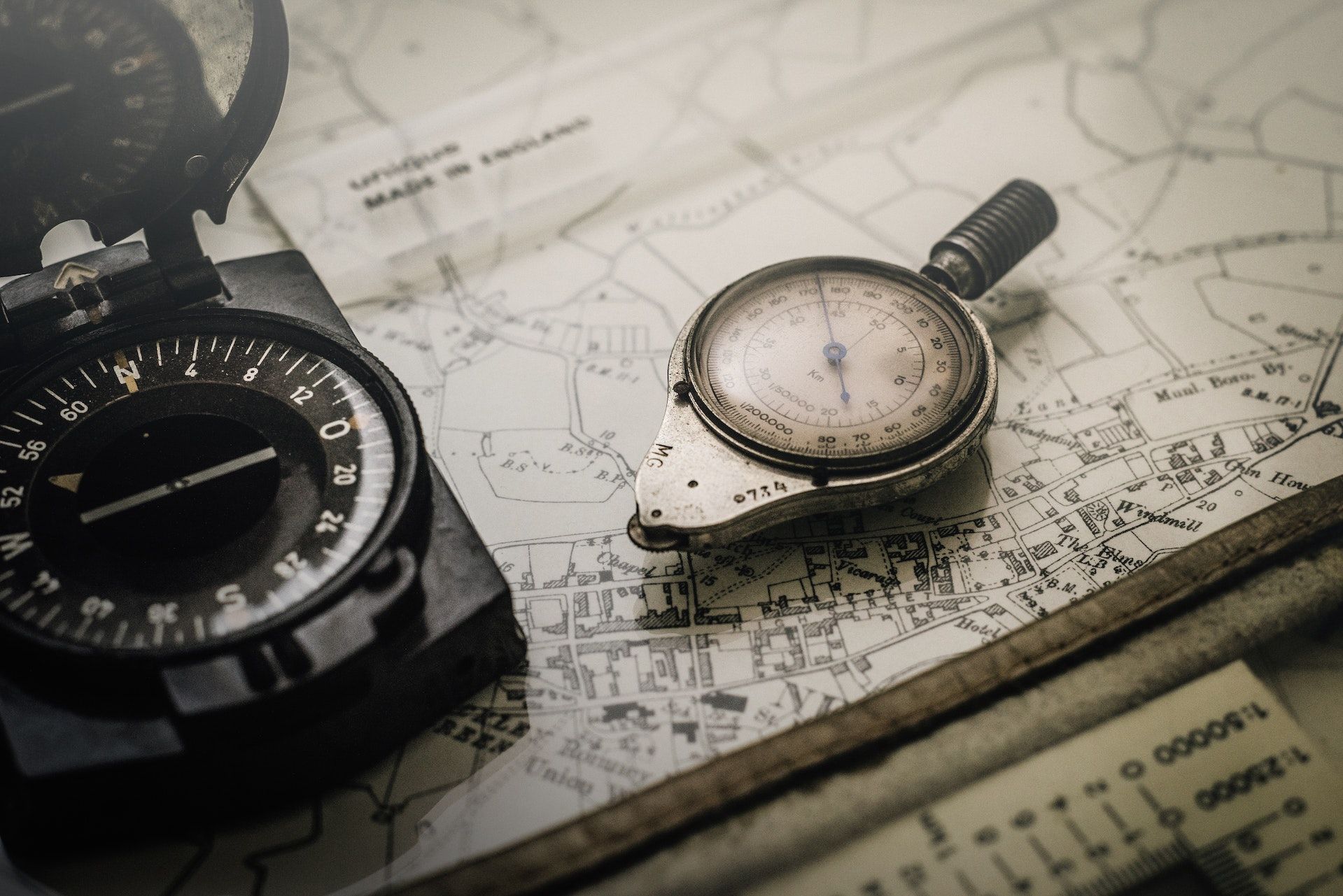 Soft-focus close-up photo compasses sitting on a map, in sepia tones